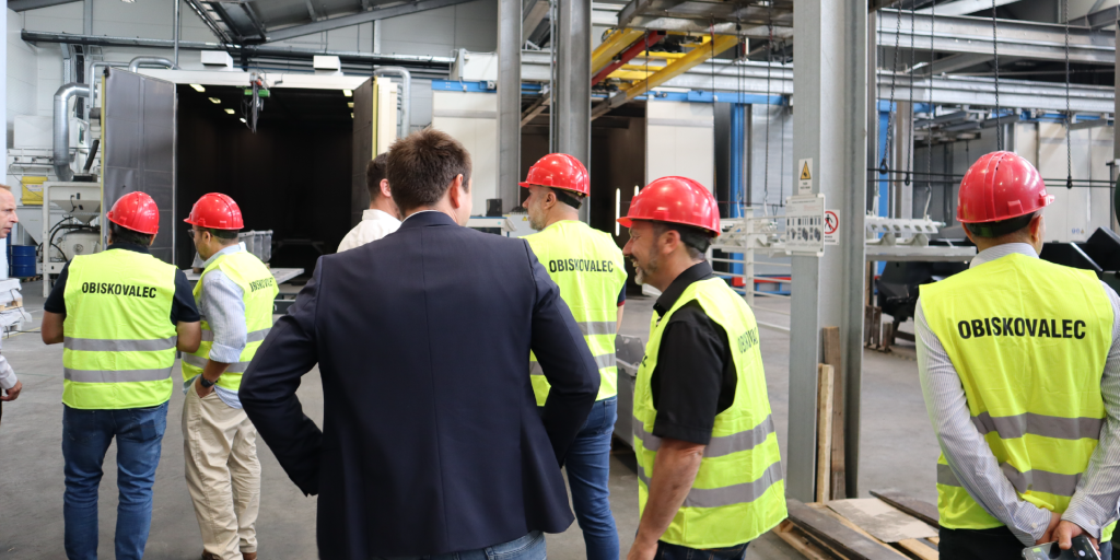 Mednarodni partnerji v odsevnih jopičih in z zaščitnimi čeladami med pogovorom o proizvodnih procesih na ogledu tovarne v sklopu dogodka Robust Distributor Event 2026.